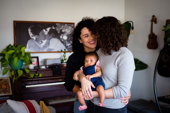 Female couple in love with their baby daughter in the living room, vertical