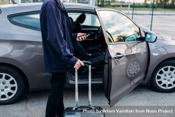 Man about to enter car with suitcase and smartphone in hand 5w6aA0