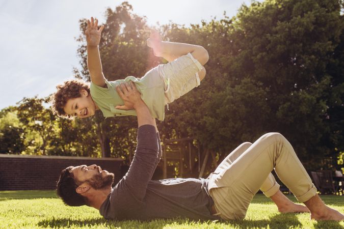 Man lying on ground and lifting his son with his arms in a park