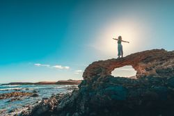 Anonymous woman with outstretched arms on cliff near sea