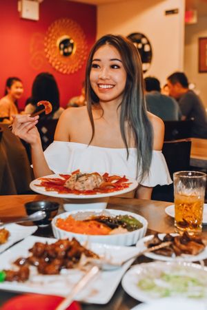 Smiling young woman eating asian food in restaurant