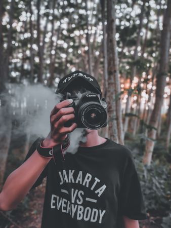 Young man holding a camera standing in the woods