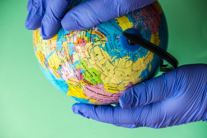 Green background with hands in blue latex gloves holding globe
