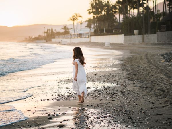 Adorable girl walking on seaside at sunset