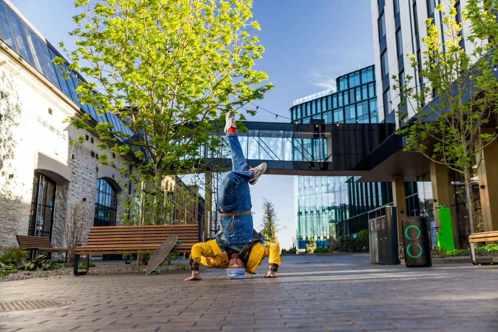 Young And Athletic B-Boy Breakdancing To Break Beats On The City Street Among Buildings Alone With A Portable Speaker.