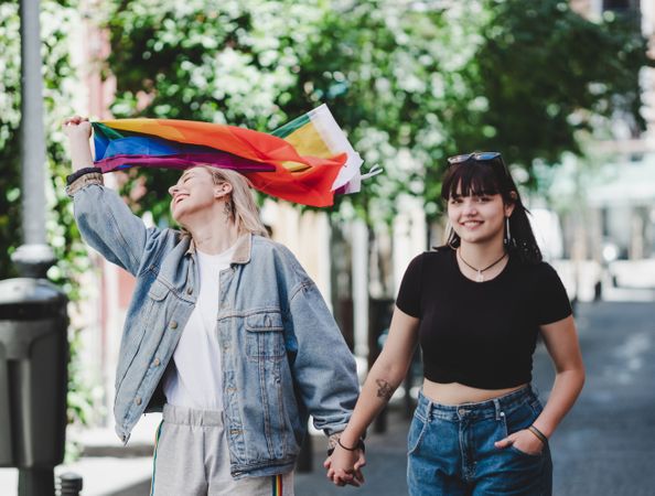 Lesbian couple with LGBT flag walking on street