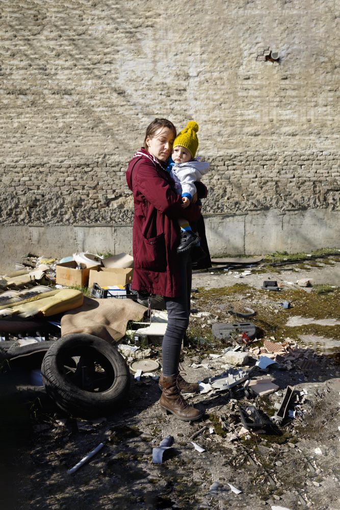 Woman holding her baby looking at rubble, vertical
