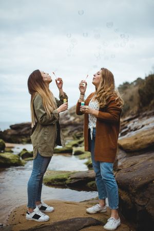Happy female friends blowing bubbles on seashore