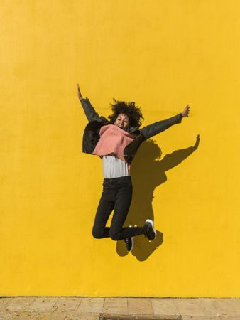 Black woman with afro hair jumping for joy in the street.
