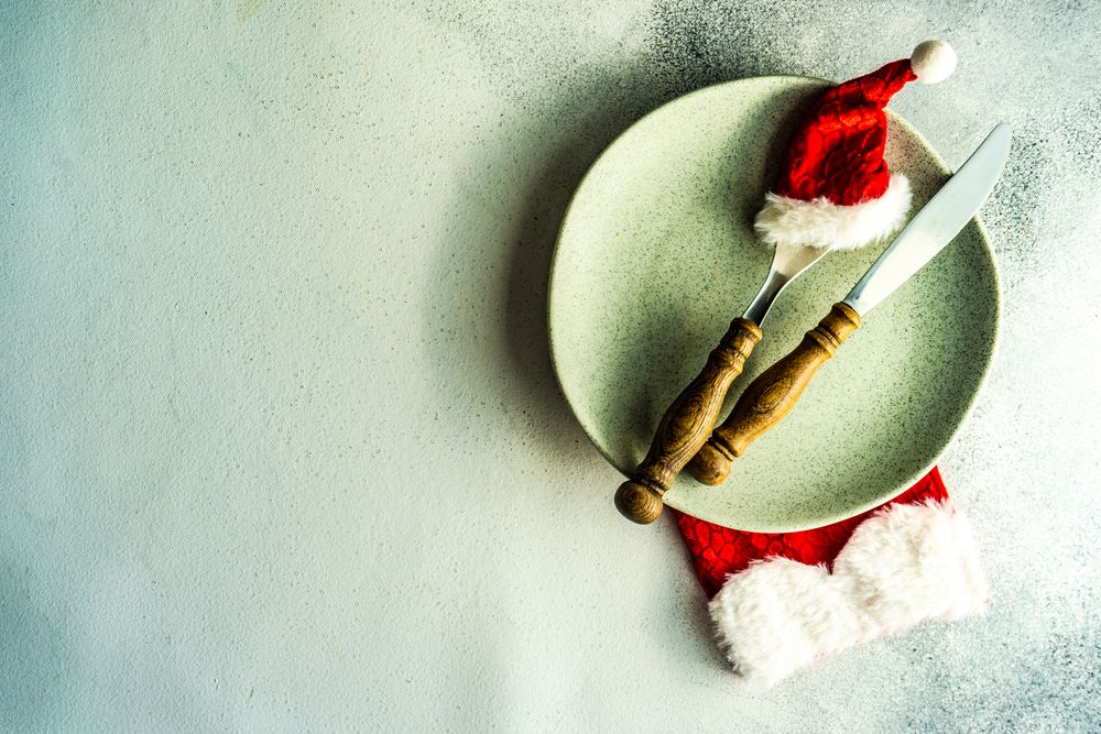 Cutlery setting with red Santa hat on silverware on light green background