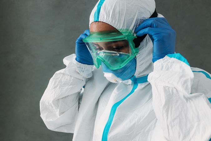 Side view of Black female medical worker putting on PPE goggles
