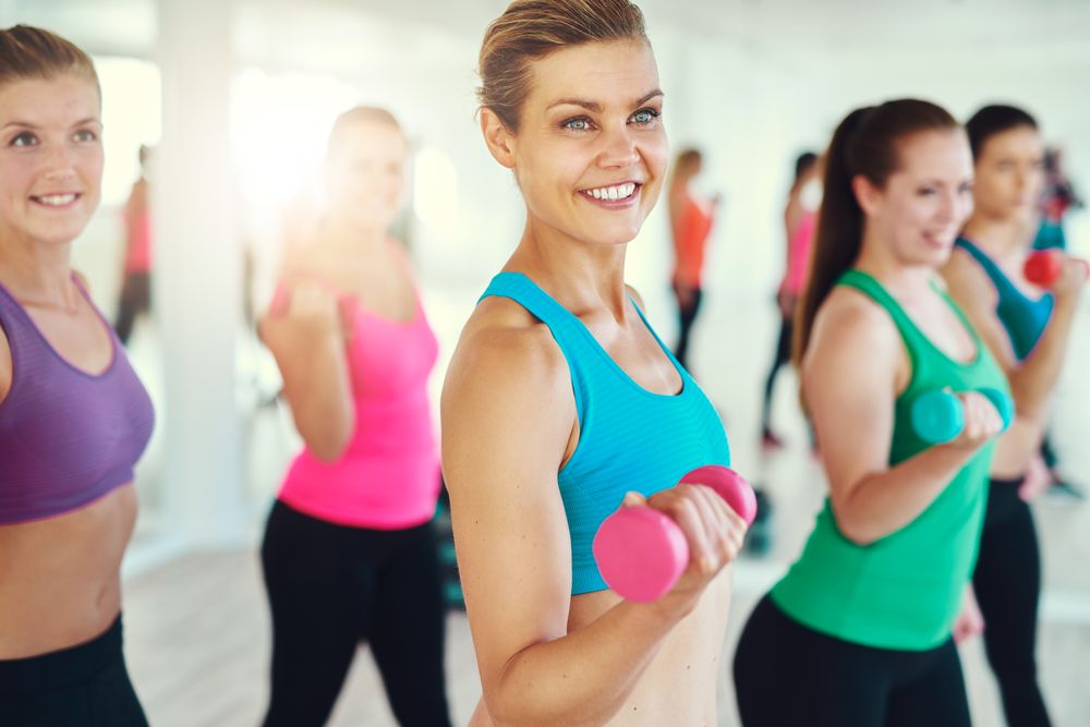 Group of women smiling while lifting weights in gym class