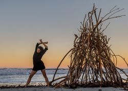 Young woman dancing on shore near water and wooden twigs placed for campfire