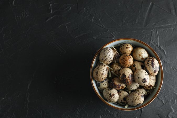 Many quail eggs in bowl on dark background, space for text and top view