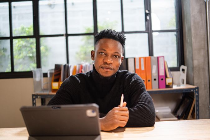 Serious Black male creative smiling and sitting at laptop in relaxed modern office