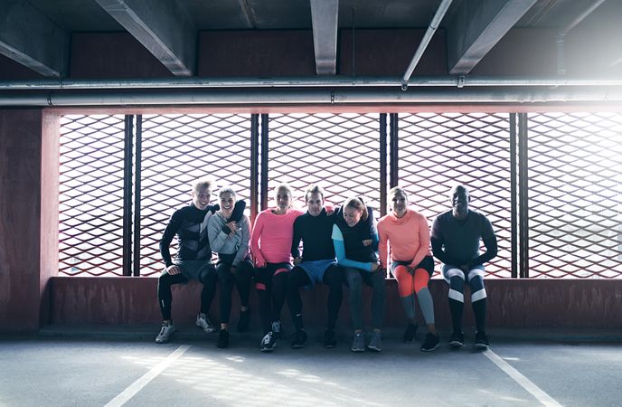Group of people in work out gear sitting on a window ledge in car park