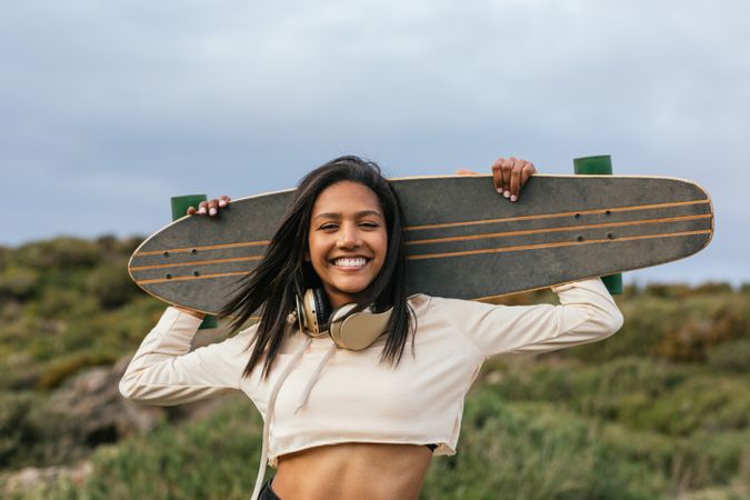 Joyful woman standing with longboard behind head