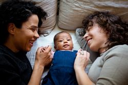 Two moms laying on bed looking at baby on the middle