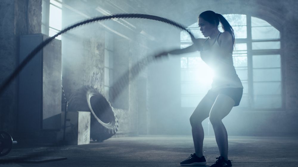 Strong Athletic Woman Exercises with Battle Ropes as Part of Her Cross Fitness Gym Workout Routine.