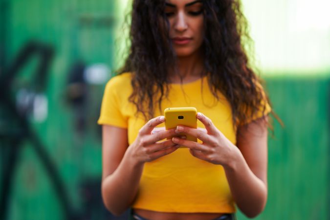 Woman with curly hair in yellow t-shirt and jeans texting on phone