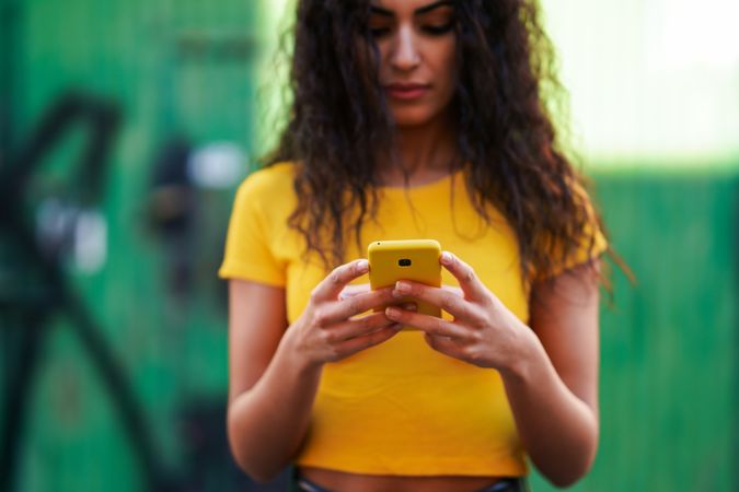 Woman with curly hair in yellow t-shirt and jeans texting on phone