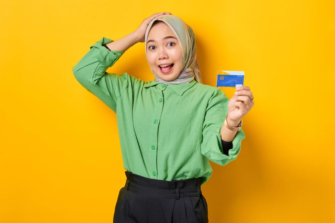 Confused Muslim woman in headscarf and green blouse holding up credit card