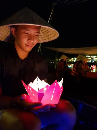 Man in conical hat holding pink lantern at night