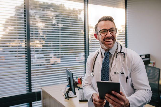 Smiling mature male doctor with digital tablet in his office