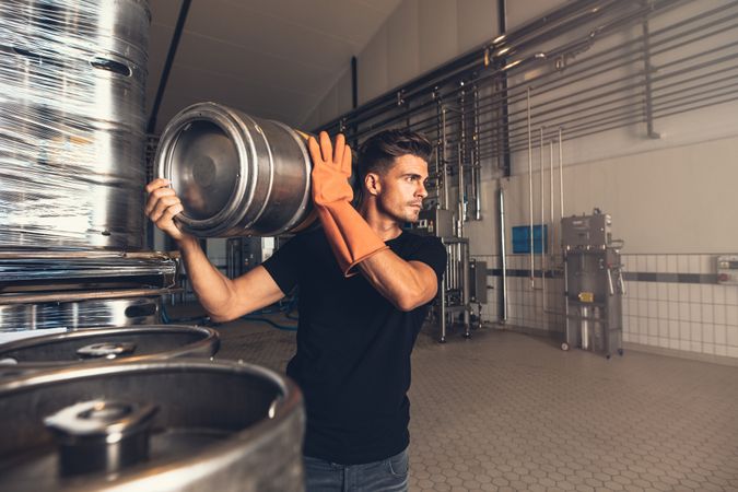 Business owner lifting metal barrel in brewery factory
