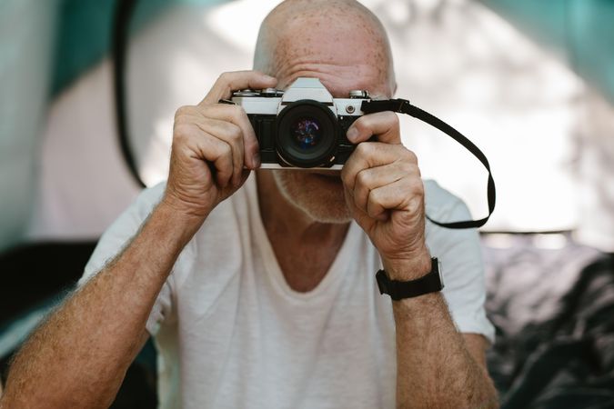 Closeup of a mature man sitting outside his camping tent and photographing with a digital camera