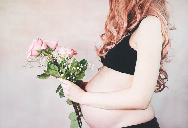 Midsection of pregnant woman with pink hair wearing crop top holding pink rose bouquet