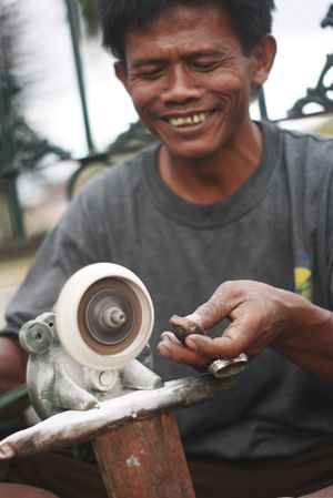 Smiling Indonesian man working on shaping an agate stone for jewelry