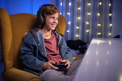 Cheerful preteen boy playing videogame with joystick in room wit