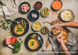 Spread of yellow lentil soup bowls, with bread, vegetable garnishes with man breaking bread 0VEPGb
