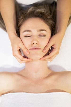Young woman with masseuse working on her chin in a spa