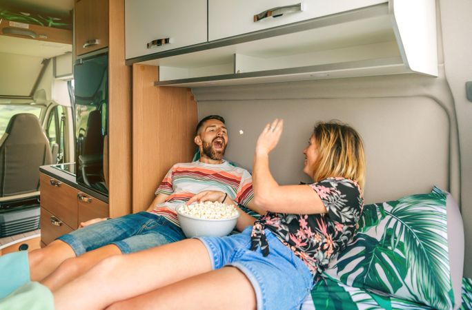 Male and female throwing popcorn at each other on a motorhome bed
