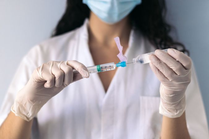 nurse with mask injecting serum into a syringe
