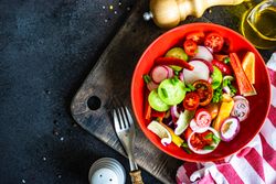 Colorful healthy raw vegetable salad served in red bowl on wooden board