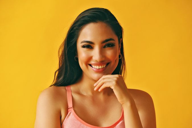 Headshot of confident happy Hispanic woman standing in front of a yellow background
