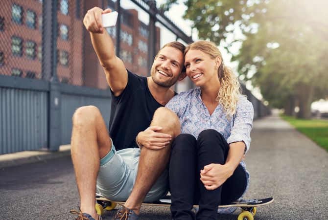 Man and woman sitting on a skateboard taking a selfie