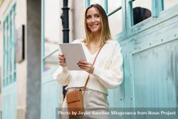Chic woman in cream standing outside with digital tablet 48BLGq