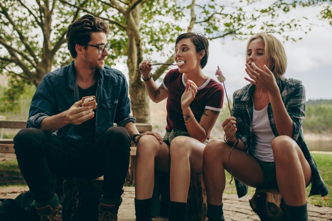 Man with two female friends camping in the countryside eating dessert