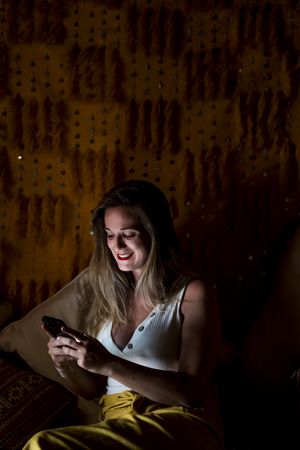 Smiling woman using smartphone in dark room