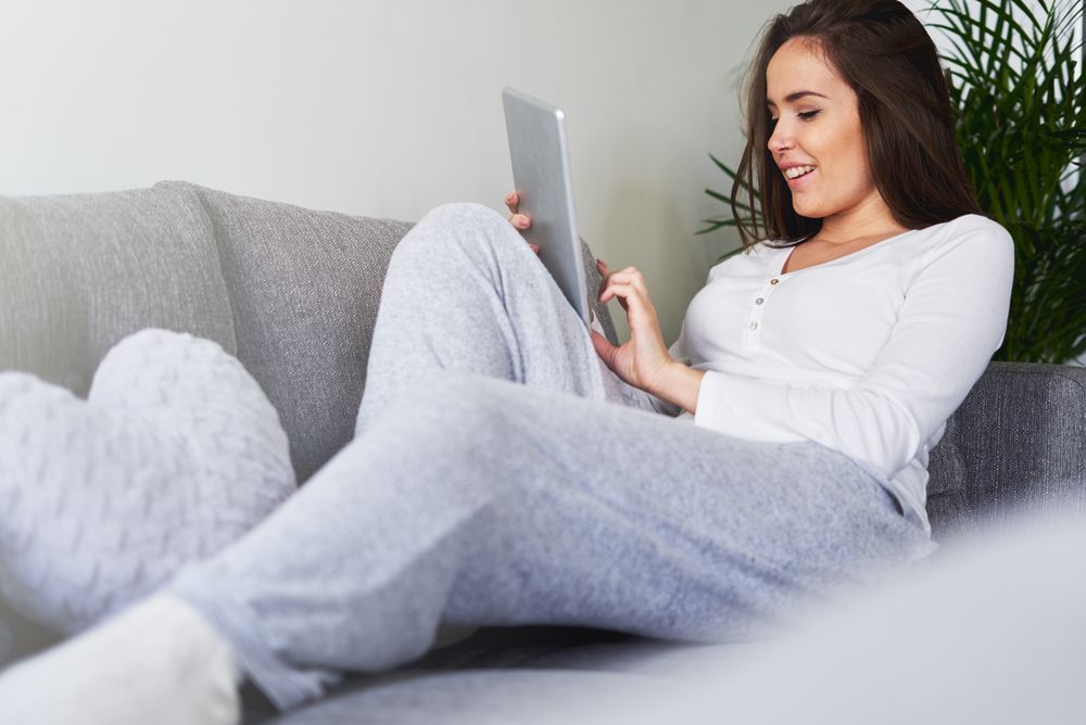Smiling woman browsing on tablet and sitting on settee