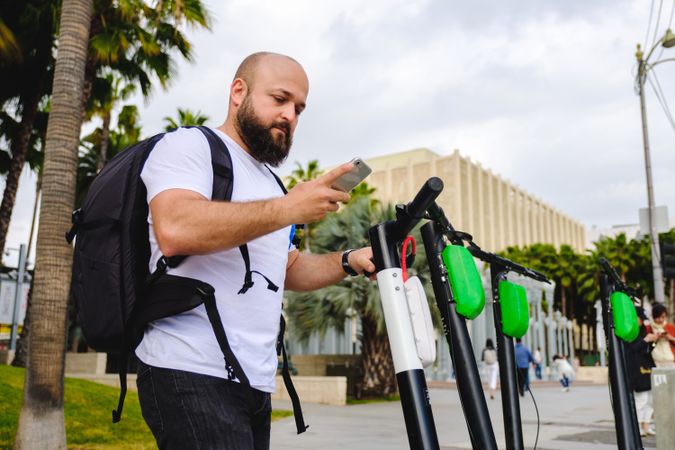 Traveler with backpack browsing smartphone and choosing electronic scooter