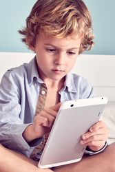 Serious boy browsing digital tablet on bed