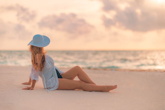 Woman siting on sand looking out at ocean, landscape shot