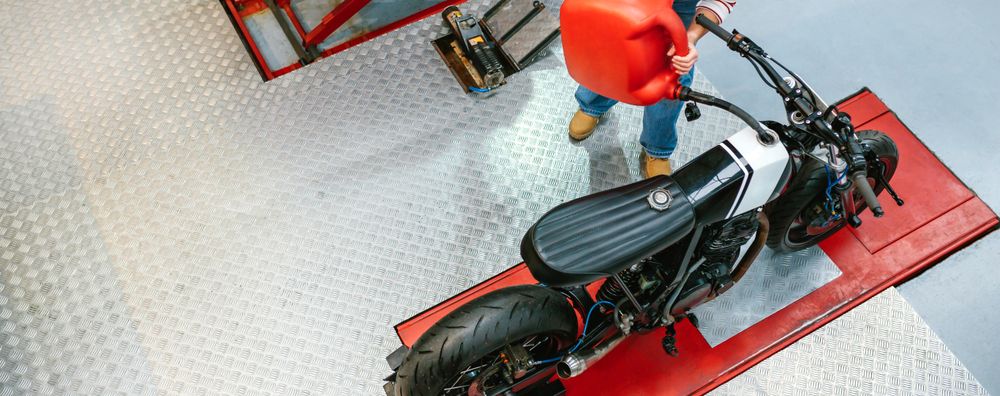 Mechanic woman with jerry can filling fuel tank of motorcycle on factory