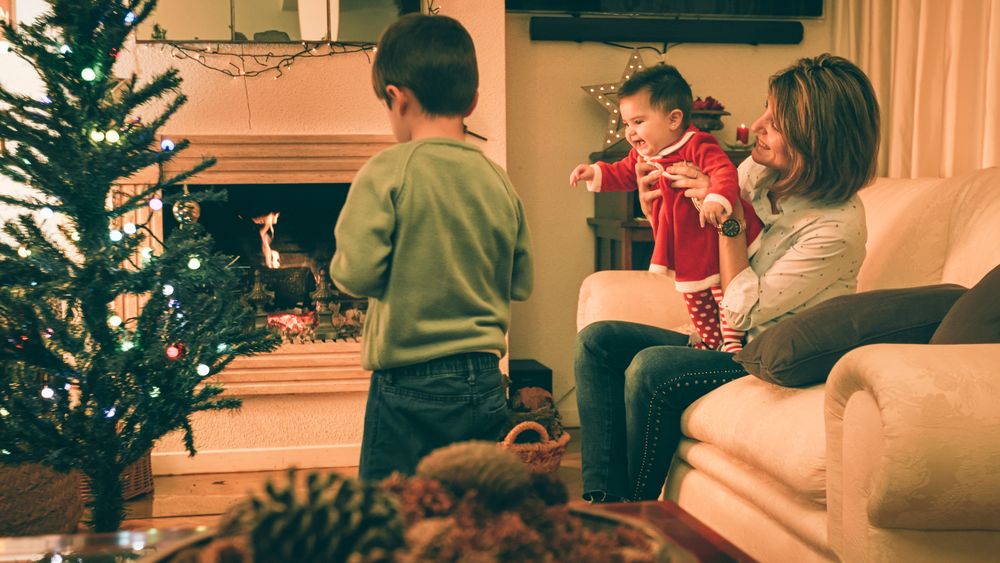 Mother playing with baby while son decorating Christmas tree