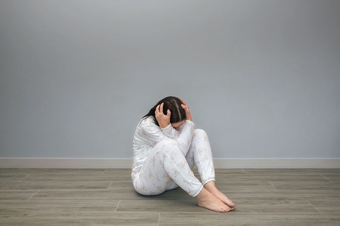 Unrecognizable woman holding head sitting on floor
